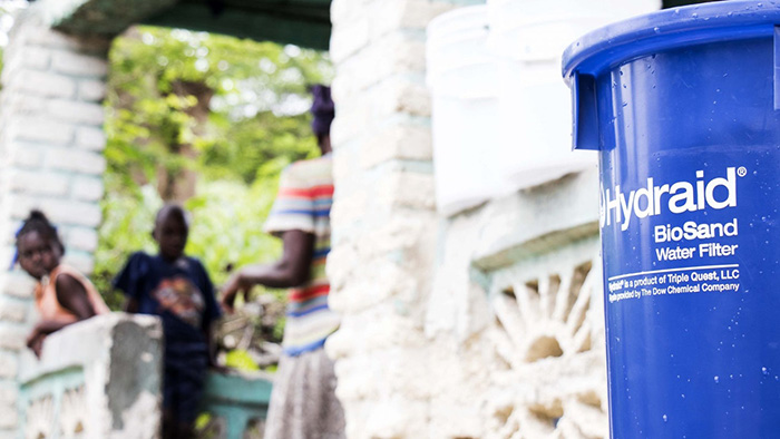 A Hydraid BioSand Water Filter with a Haitian family in the background.