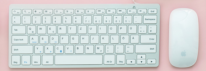 A white keyboard and a mouse on a pastel pink desk.
