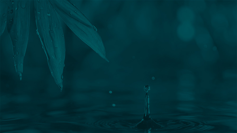 A drop of water falls onto a body of water with a leaf in the top left corner