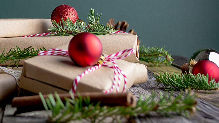 Packages wrapped in brown paper and red and white twine with baubles and pine branches around them.