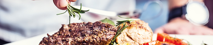A chef garnishes a steak with a sprig of rosemary.