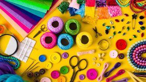 Brightly coloured thread, buttons, scissors, fabric, ribbons, and other sewing implements against a yellow background