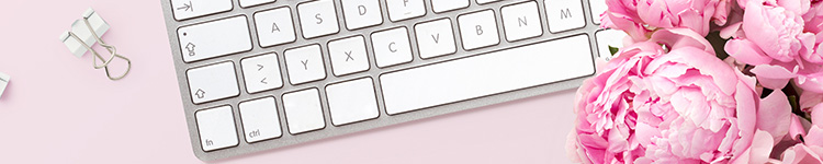 A keyboard on a pink surface, next to a bouquet of flowers and a few paper clips