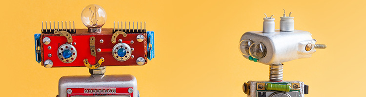 Two toy robots against an orange-yellow background. The one on the left is red and made of spare parts and the one on the right is silver, made of spare parts, and is looking at the other one.